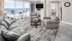 A living room with a sofa, armchair, and coffee table, a TV mounted on the wall, and a view of the ocean through large sliding doors. - Island Princess 604 Beachfront Luxury with Stunning Gulf Views! (Fort Walton Beach)