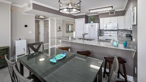 A modern kitchen with a granite countertop, stainless steel appliances, and a dining area with a glass table and wooden chairs. - Island Princess 604 Beachfront Luxury with Stunning Gulf Views! (Fort Walton Beach)