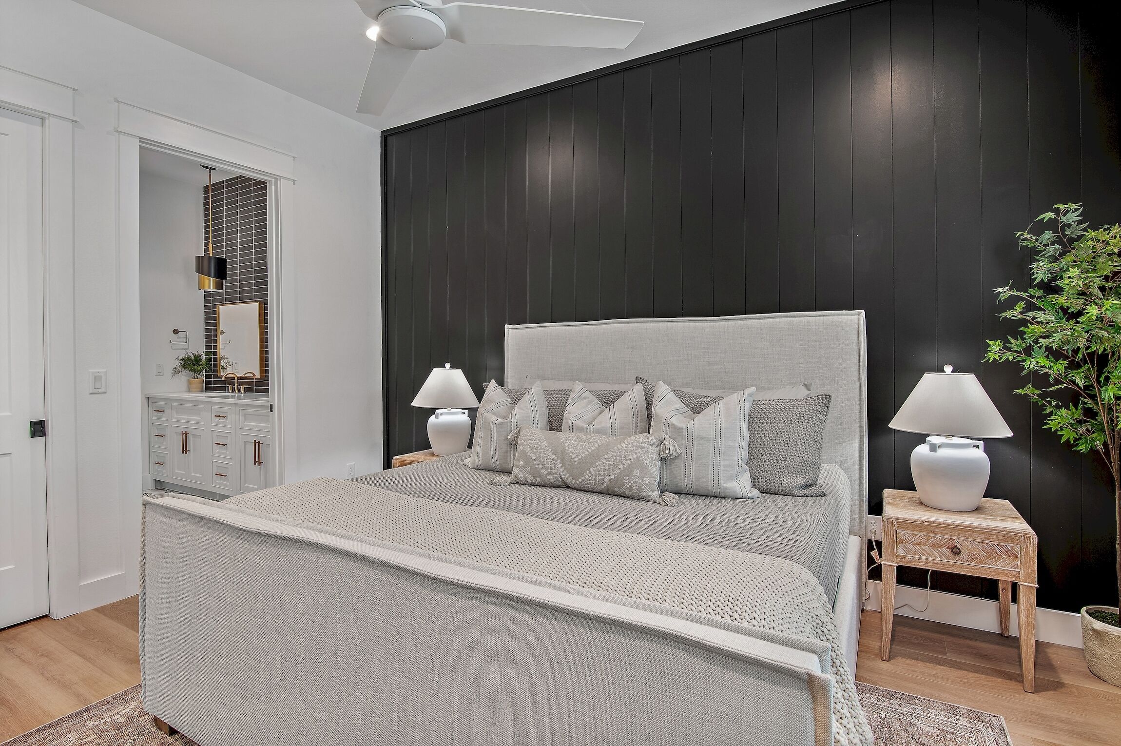 A modern bedroom with a large bed, bedside lamps, a small wooden nightstand, and a potted plant.