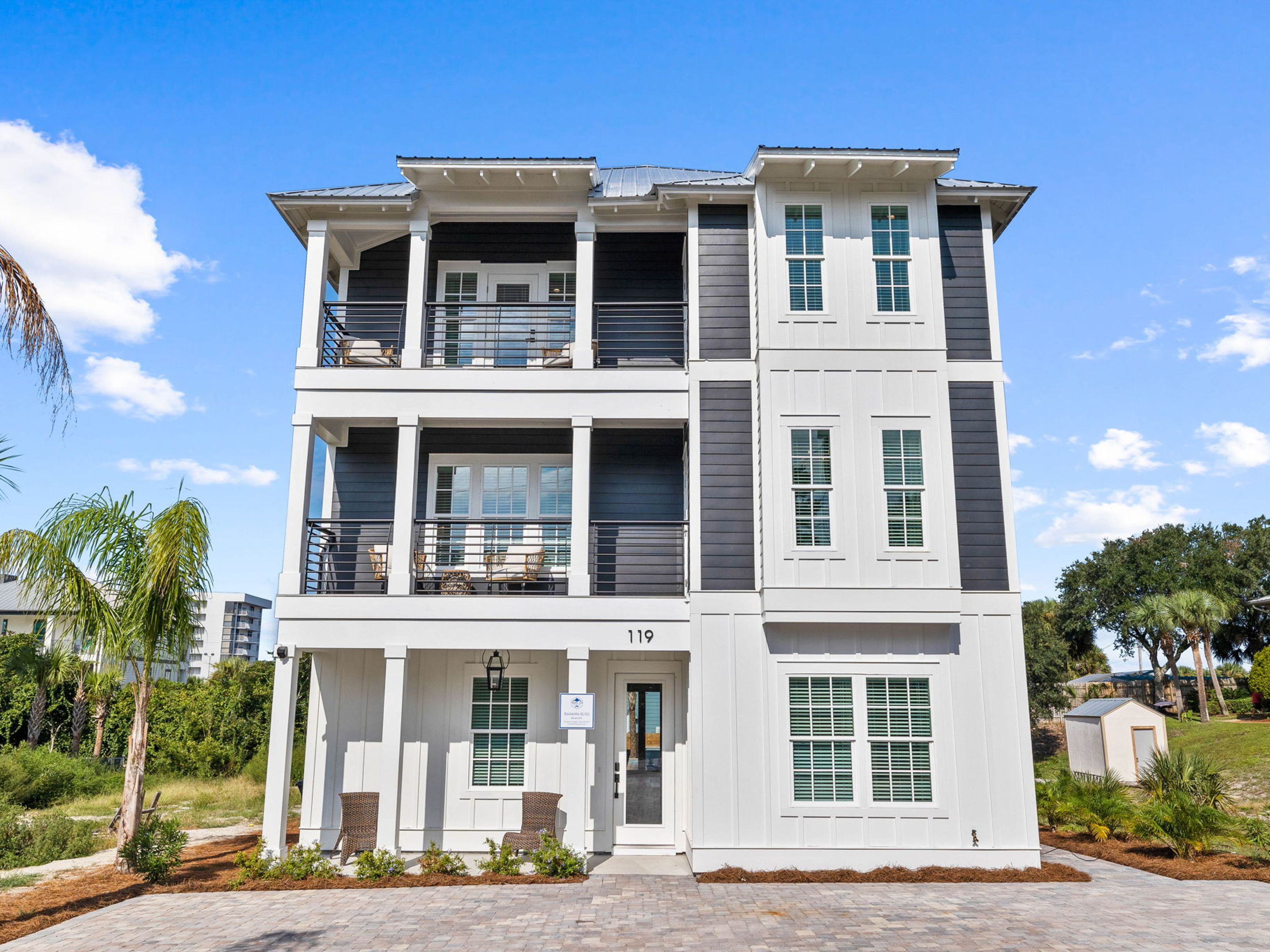 A multi-story residential building with a balcony on the second floor, a front entrance, and a small garden area.