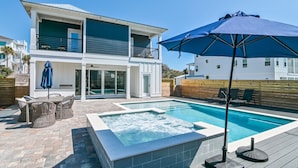 A modern two-story house with a swimming pool, outdoor seating, and a large umbrella.