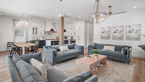A spacious living room with grey sofas, a wooden coffee table, and a dining area with a wooden table and chairs.