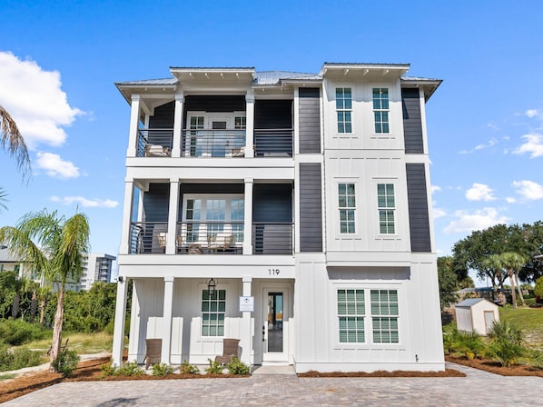 A multi-story residential building with a balcony on the second floor, a front entrance, and a small garden area.
