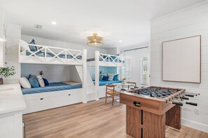 A room with bunk beds, a foosball table, and a window with blinds.
