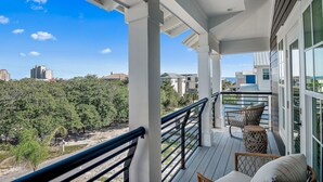 A covered balcony with wicker furniture, a railing, and a view of a cityscape and greenery.