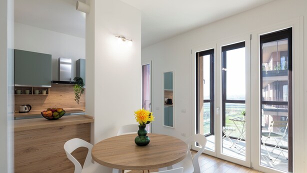A modern kitchen with a wooden countertop, a bowl of fruit, and a vase with flowers. There is a dining area with a round table and white chairs. - notaMi - Sei Milano Suite (Milan)