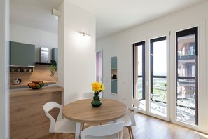 A modern kitchen with a wooden countertop, a bowl of fruit, and a vase with flowers. There is a dining area with a round table and white chairs. - notaMi - Sei Milano Suite (Milan)