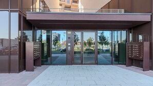 A modern building entrance with glass doors, a metal canopy, and a parking area visible in the background. - notaMi - Sei Milano Suite (Milan)