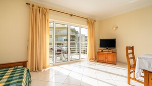 Ein Hotelzimmer mit Bett, Fernseher, Esstisch, Stuhl, Holzschrank und einer Glastür zum Balkon.