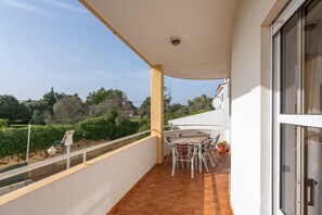 Un balcon avec une table et des chaises, un pot de fleurs et une vue sur la verdure et les bâtiments.