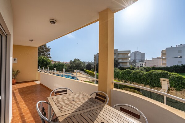 Ein Balkon mit Holztisch und -stühlen, Blick auf einen Pool und umgebende Gebäude.