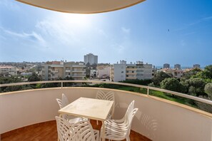 Un balcón con mesa y sillas, con vistas a un paisaje urbano con edificios y zonas verdes.