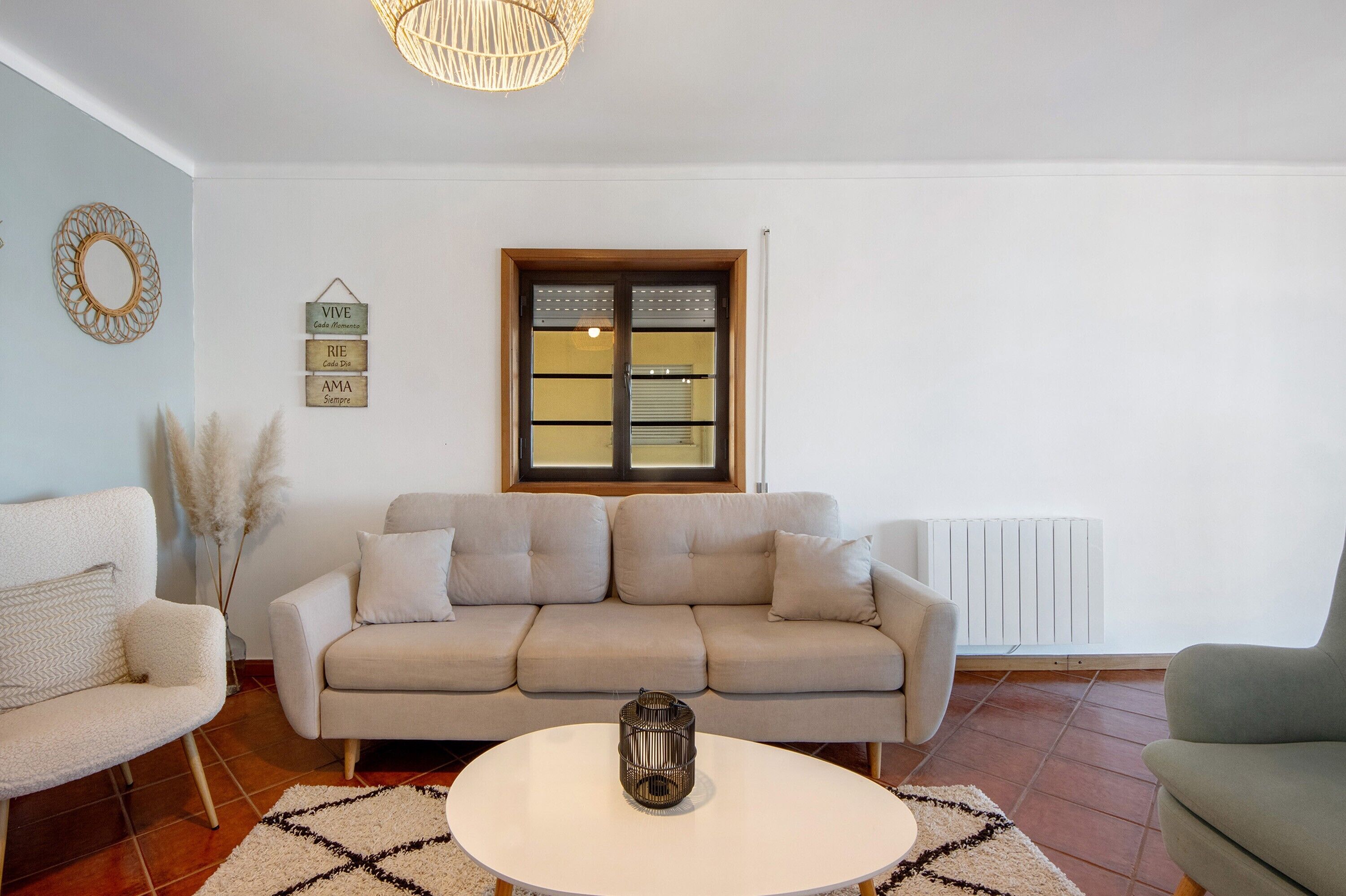 Un soggiorno con un divano color beige, un tavolino da caffè bianco, uno specchio decorativo e una finestra con persiane.