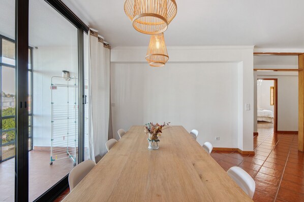 Un coin repas avec une table en bois, des chaises blanches, un vase de fleurs et un luminaire suspendu.