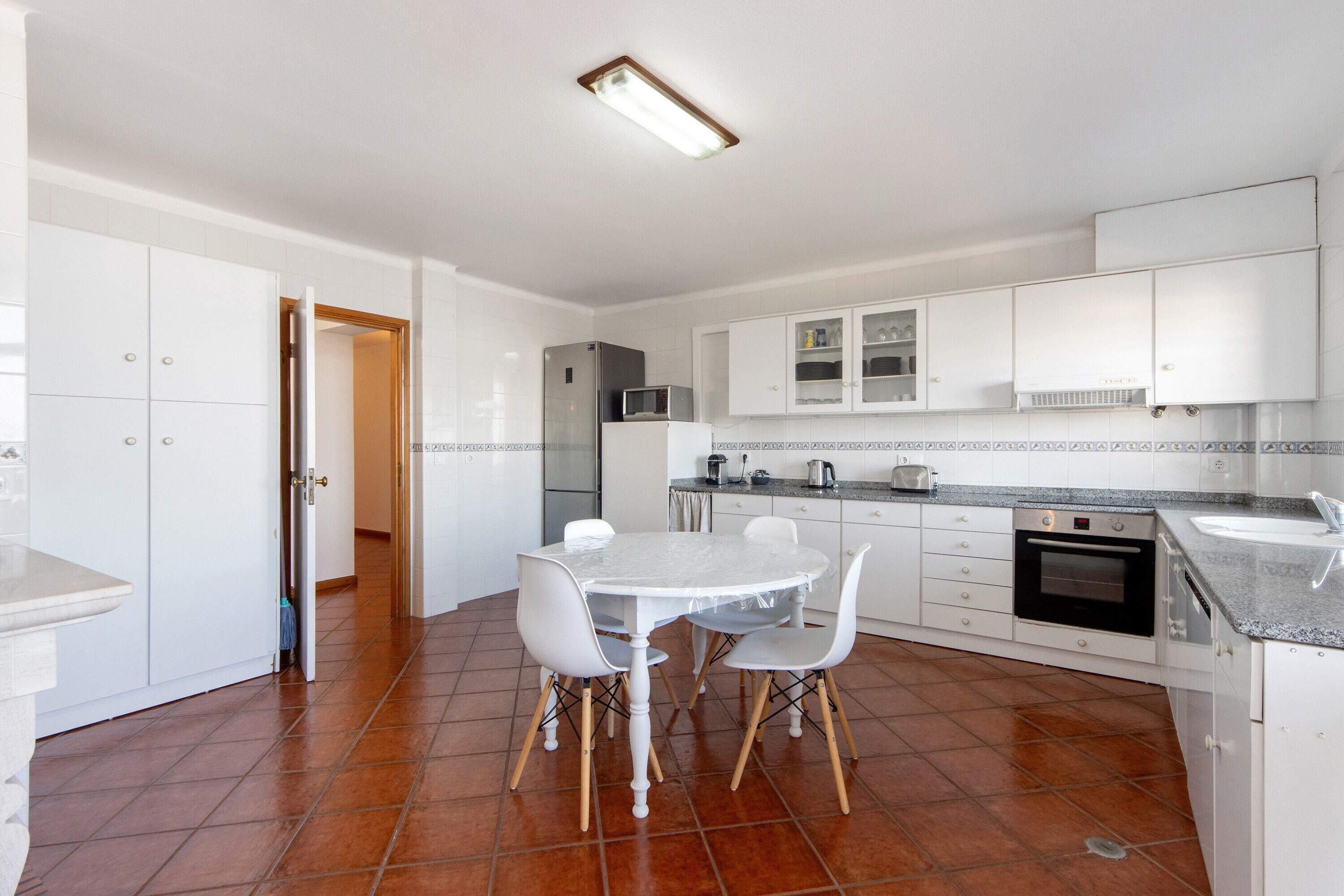 Una cocina con armarios blancos, una mesa de comedor con sillas, un refrigerador, un microondas y un horno.
