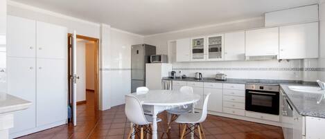 Una cocina con armarios blancos, una mesa de comedor con sillas, un refrigerador, un microondas y un horno.