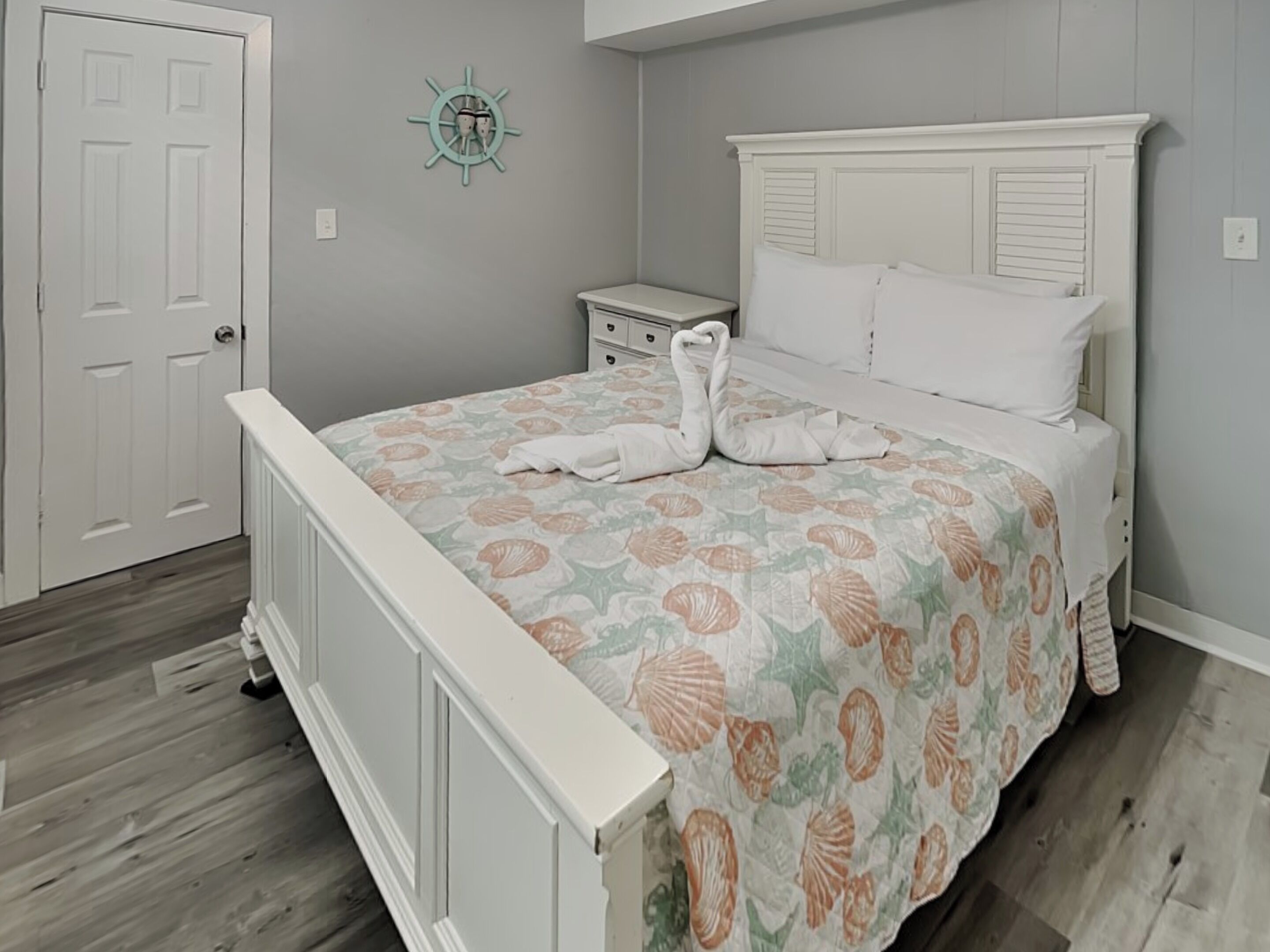 Un dormitorio con cama, mesita de noche, reloj de pared y puerta.