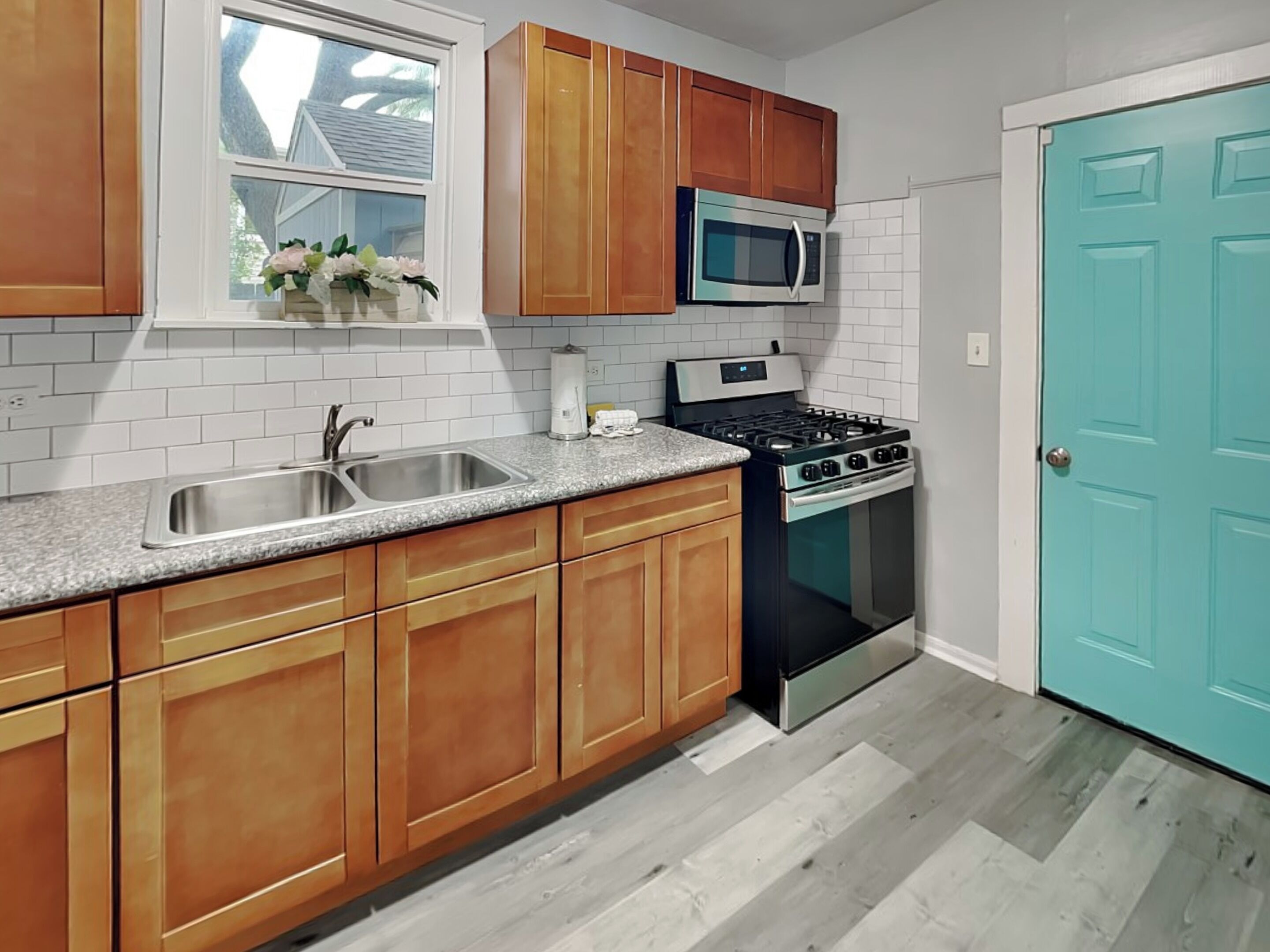 Una cocina con armarios de madera, un lavamanos de acero inoxidable, un microondas y una estufa.