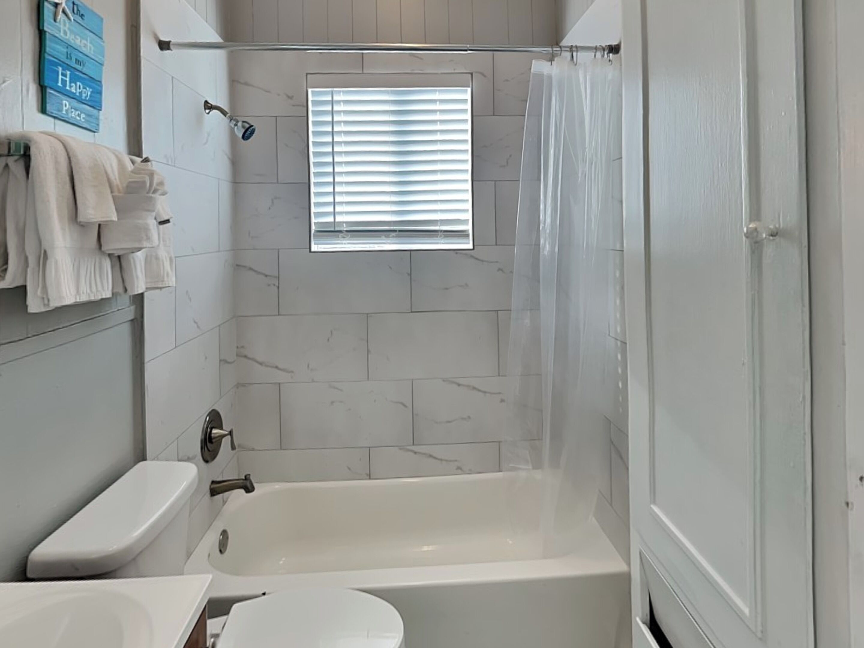 A bathroom with a bathtub, toilet, and a window with blinds.