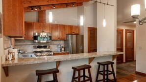A kitchen with wooden cabinets, stainless steel appliances, a granite countertop, and bar stools. - Palisades and North Star Ski Apres at St. Francis (Tahoe City)