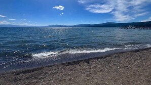 A beach with clear water, a wooden pier, and distant mountains. - Palisades and North Star Ski Apres at St. Francis (Tahoe City)