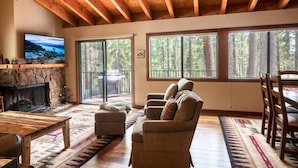A cozy living room with a stone fireplace, a television, a sofa, and a dining area with a table and chairs. - Palisades and North Star Ski Apres at St. Francis (Tahoe City)