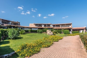 Un patio con un sendero empedrado, una roca grande y un edificio con techo de tejas y balcones.