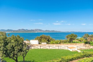 A coastal landscape with a clear view of the sea, a grassy area, and a building with a fenced courtyard. - Ceraso Sunset (Olbia)