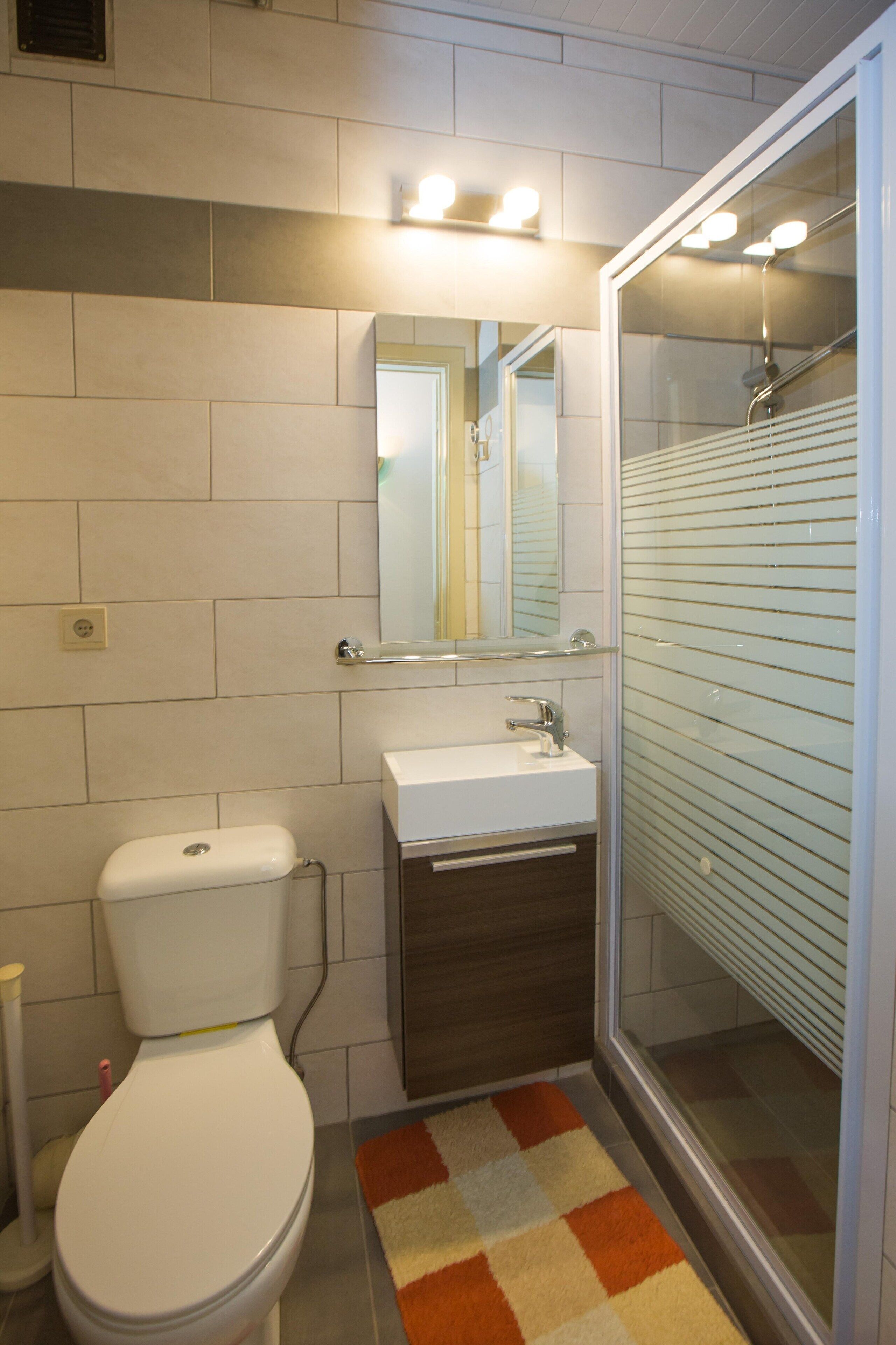 A bathroom with a toilet, sink, mirror, and shower.