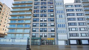Un edificio de varios pisos con fachada de vidrio, varios balcones y locales comerciales en la planta baja, incluyendo una cafetería y un restaurante.