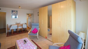 Una sala de estar con sofá, una mesa de comedor con sillas, un armario de madera y un espejo.