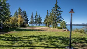 Un parc avec une pelouse, un lampadaire en métal et une vue sur un lac, avec des arbres et des montagnes en arrière-plan.