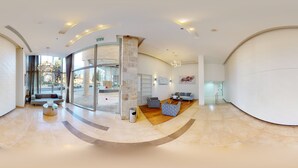 A spacious lobby with a curved floor, a glass entrance, a seating area with sofas, and a wall-mounted artwork. - ♦King David Residences♦Stunning 2-Bdr with Balcony & Views♦ (Jerusalem)