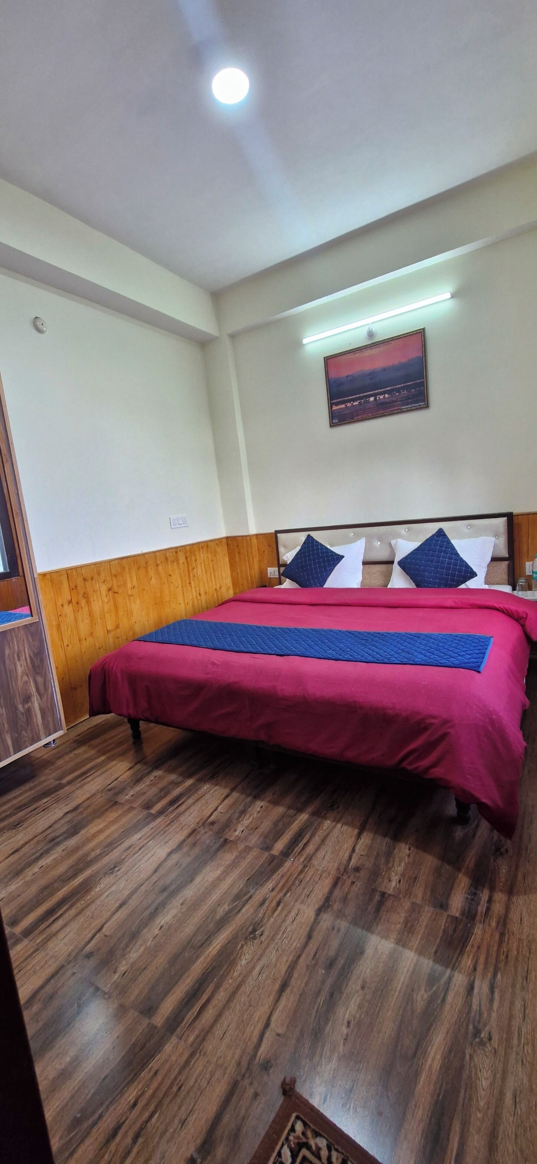 Une chambre d’hôtel avec un plancher en bois, un lit recouvert d’une courtepointe rouge et bleue, et un tableau accroché au mur.