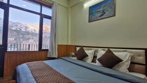 A bedroom with a large window, wooden walls, a bed with a quilted blanket, and a painting on the wall. - White Villa (Shimla)
