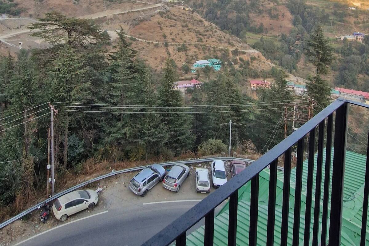 A balcony with a view of a hillside town, a road with parked cars, and a green-roofed building.