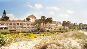 A hotel with multiple balconies, a central courtyard with palm trees, and a sandy beach area. - Studio in Marbella With Beachfront Pool (Marbella)