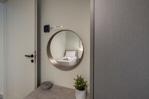 A bathroom with a round mirror, a towel rack, a potted plant, and a door. - Athena - 2 Bedroom Apartment Argostoli (kefalonia)