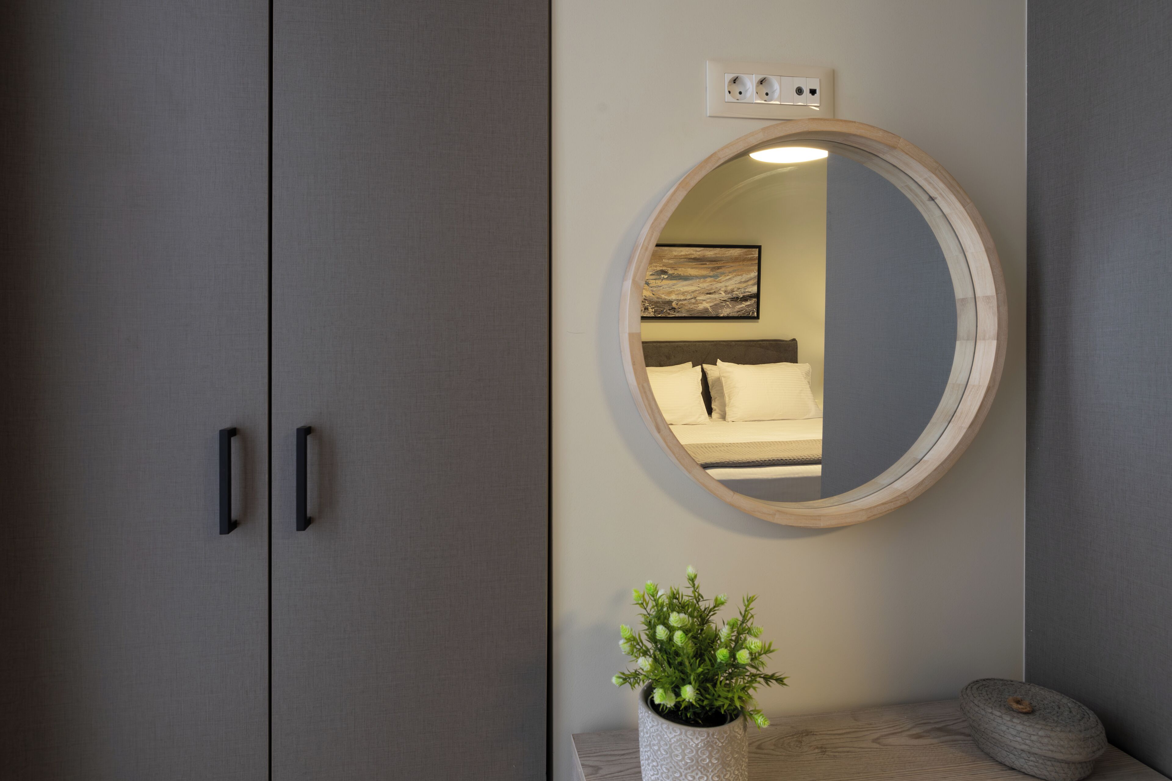 A bedroom with a round mirror, a bedside plant, and a wooden bedside table.