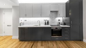 A modern kitchen with grey cabinets, a white countertop, and a built-in oven. - Modern London Nell Gwynn House Apartment (London)