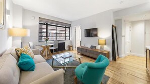 A modern living room with a sofa, a teal armchair, a coffee table, and a TV mounted on the wall. - Modern London Nell Gwynn House Apartment (London)