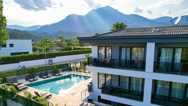 Uma casa moderna de dois andares com piscina, cercada por vegetação exuberante e montanhas ao fundo.