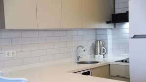 Uma cozinha moderna com armários brancos, uma pia de aço inoxidável e uma chaleira.