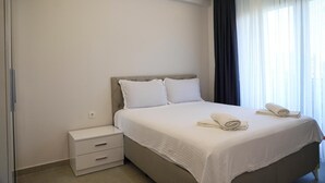 Quarto de hotel moderno com uma cama grande, roupa de cama branca, uma mesa de cabeceira e uma janela com cortinas.