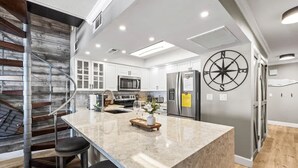 Een moderne keuken met een centraal eiland, roestvrijstalen apparatuur en een houten trap.