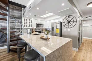 Une cuisine moderne dotée d’un îlot central, d’appareils électroménagers en acier inoxydable et d’un escalier en bois.