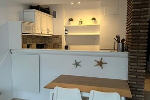 A kitchen with white cabinets, a microwave, and a stove. There are two starfish decorations on the wall and a brick wall on the right. - Studio in Estepona Near Sandy Beach (Estepona)