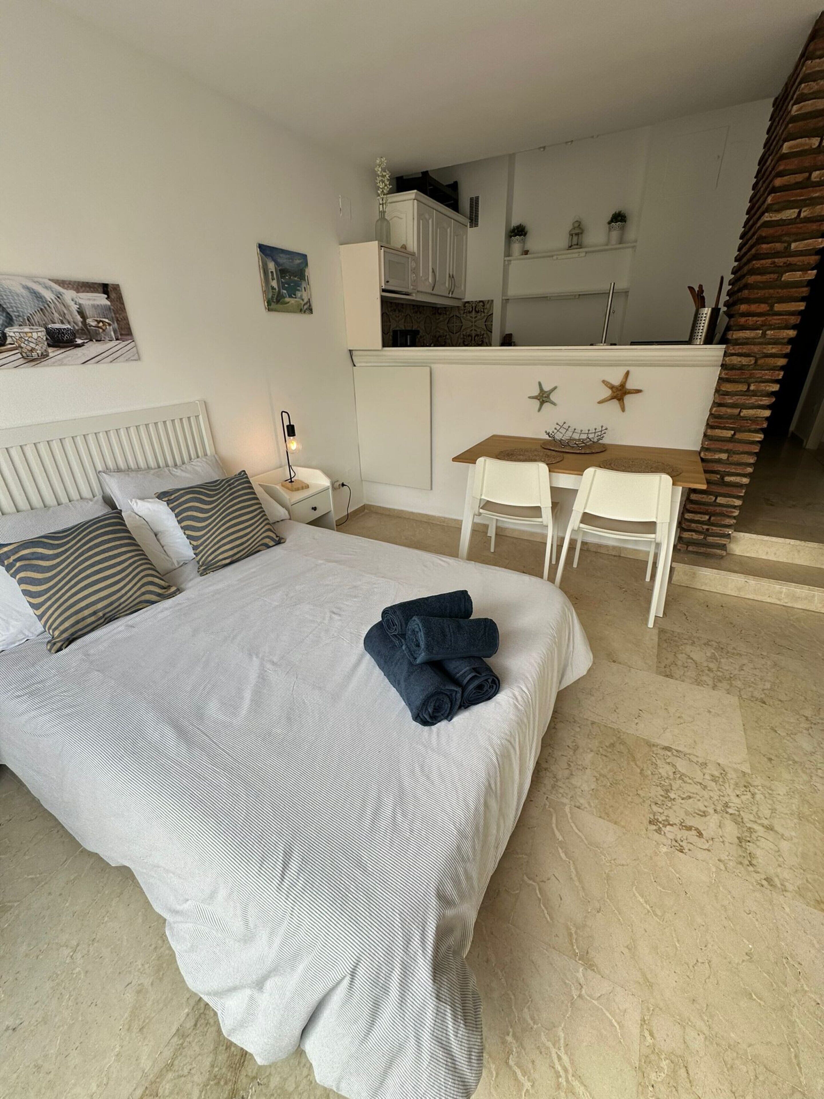 Une chambre avec un lit, un bureau et une chaise. Il y a un petit coin cuisine avec des placards et un évier.