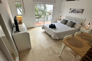 A bedroom with a bed, a desk, a chair, a table, and a balcony with a view of greenery. - Studio in Estepona Near Sandy Beach (Estepona)