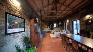 Een rustiek interieur met een lange eettafel, houten balken, stenen muren en een lijst met een afbeelding van Porto, Portugal.